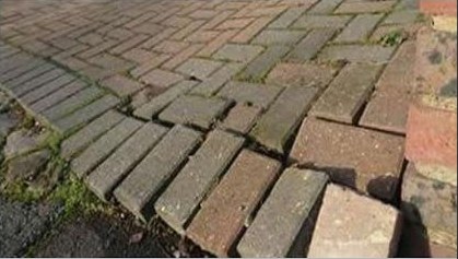 Paver pavement with opened edge restraint and displaced blocks, before repair